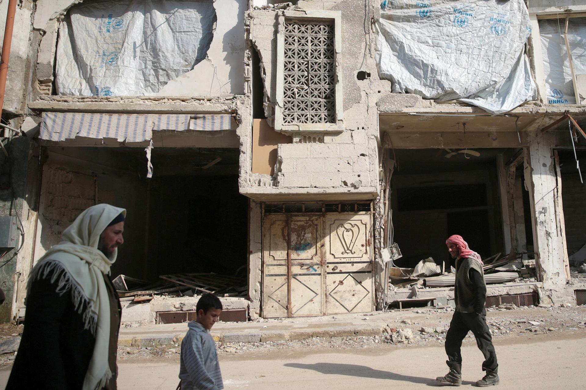 People walk past a damaged building in the eastern Damascus suburb of Ghouta, Syria.