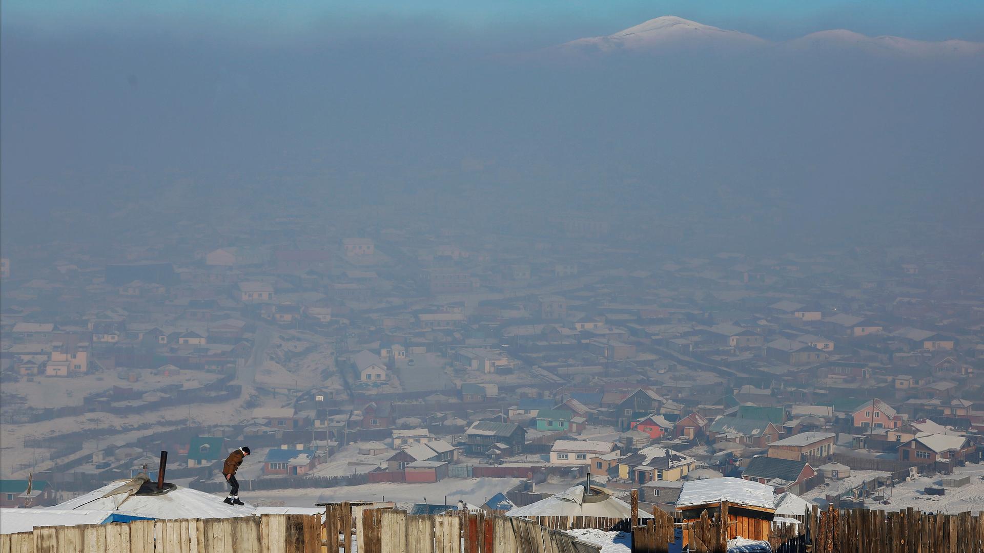 A man walks on the roof of a traditional ger home while fixing the chimney of a coal burning stove on a cold hazy day on the outskirts of Ulaanbaatar, Mongolia.