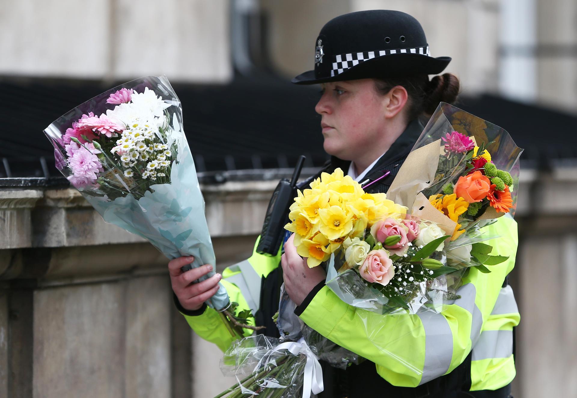 A police officer carries bouquets of flowers on Whitehall the morning after an attack in London.