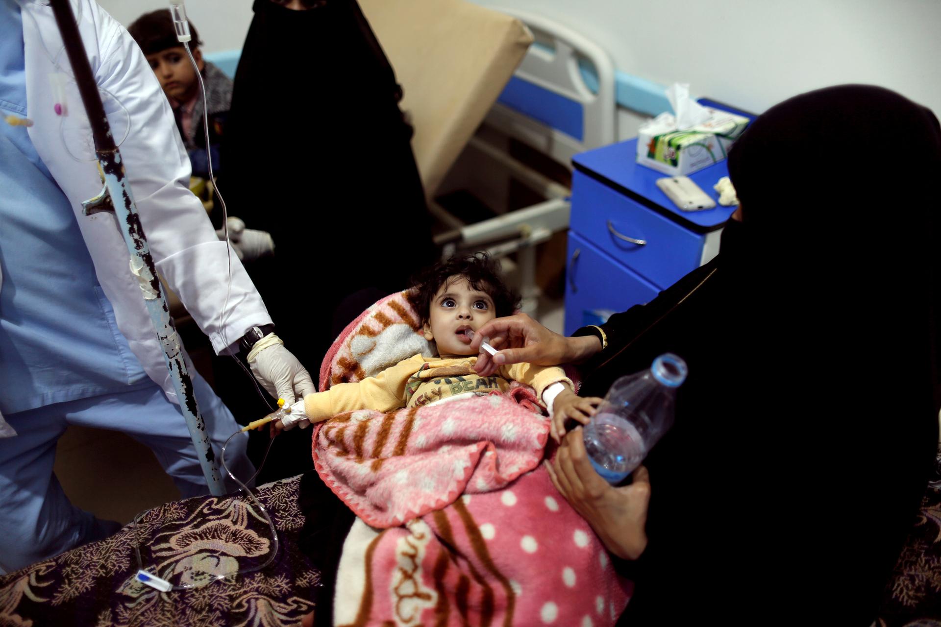 Woman leans over hospital bed to give her daughter rehydration fluid at a cholera treatment center in Sanaa.