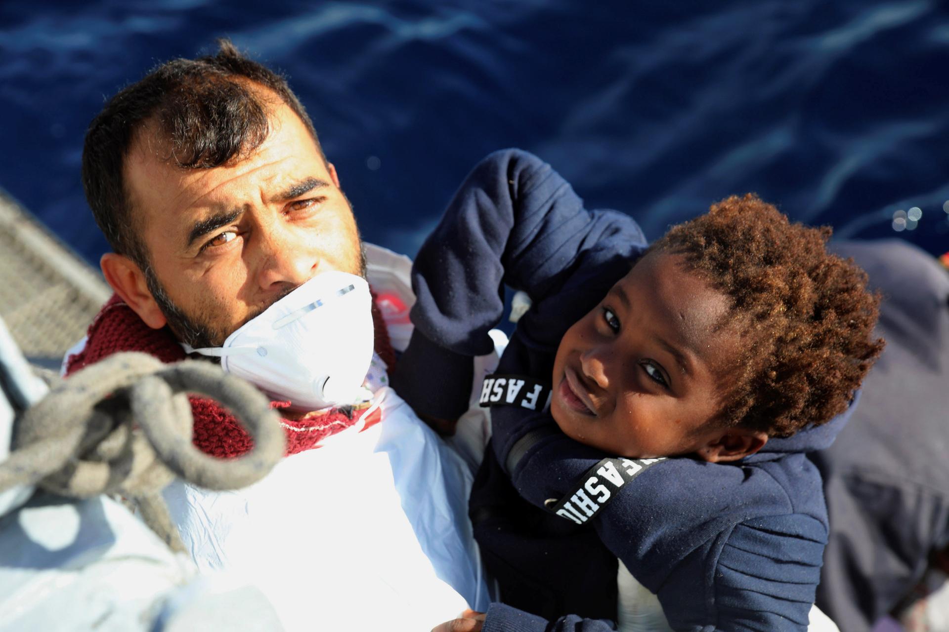 Man on a boat lifting a young child to hand to rescuers