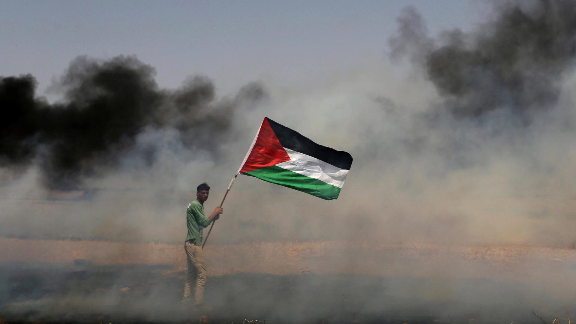 A demonstrator holds a Palestinian flag during clashes with Israeli troops at a protest where Palestinians demand the right to return to their homeland, near the Israel-Gaza border in the southern Gaza Strip on April 13, 2018.