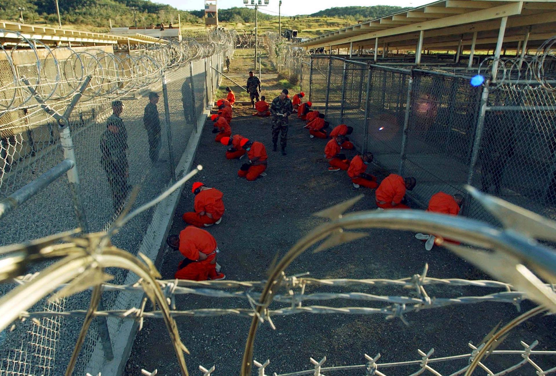 Detainees in orange jumpsuits sit in a holding area under the watchful eyes of military police during inprocessing at the temporary detention facility at Guantanamo Bay's Camp X-Ray in this January 11, 2002 file photograph.