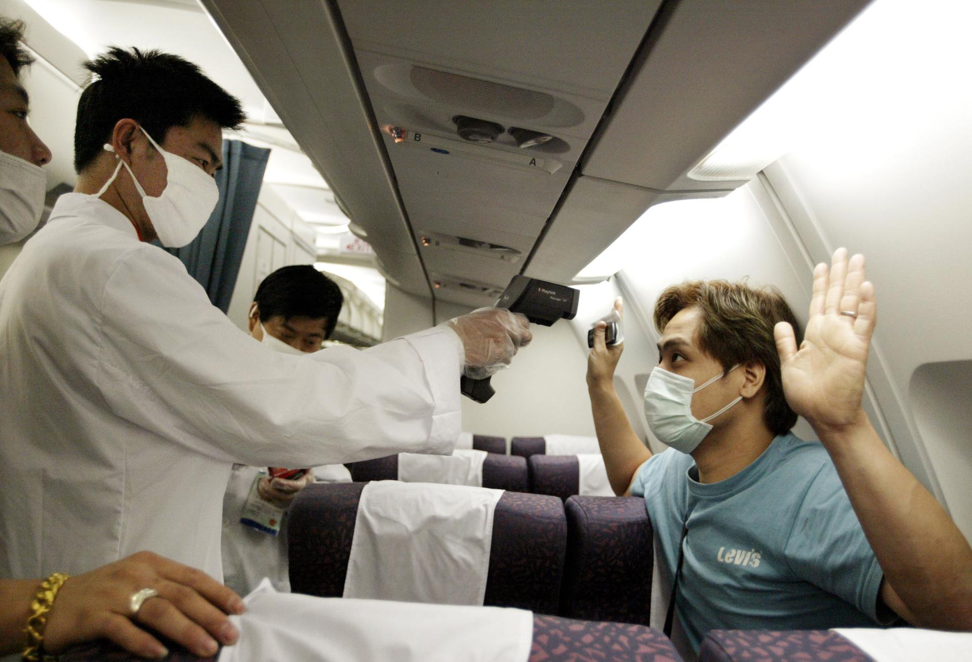 A Chinese doctor checks the temperature of a passenger on a flight from Hong Kong to Shanghai during the SARS outbreak in 2003. There are now fears that Ebola could spread via travel from West Africa to the rest of the world.