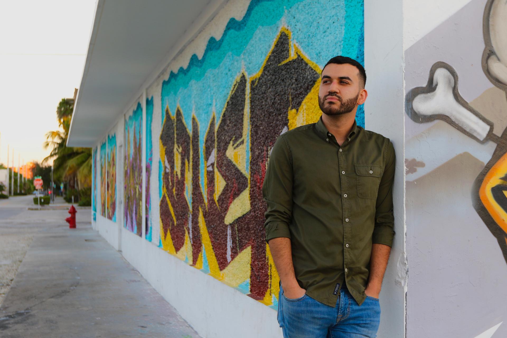 A man leans on a colorfully painted wall and looks over his right shoulder.