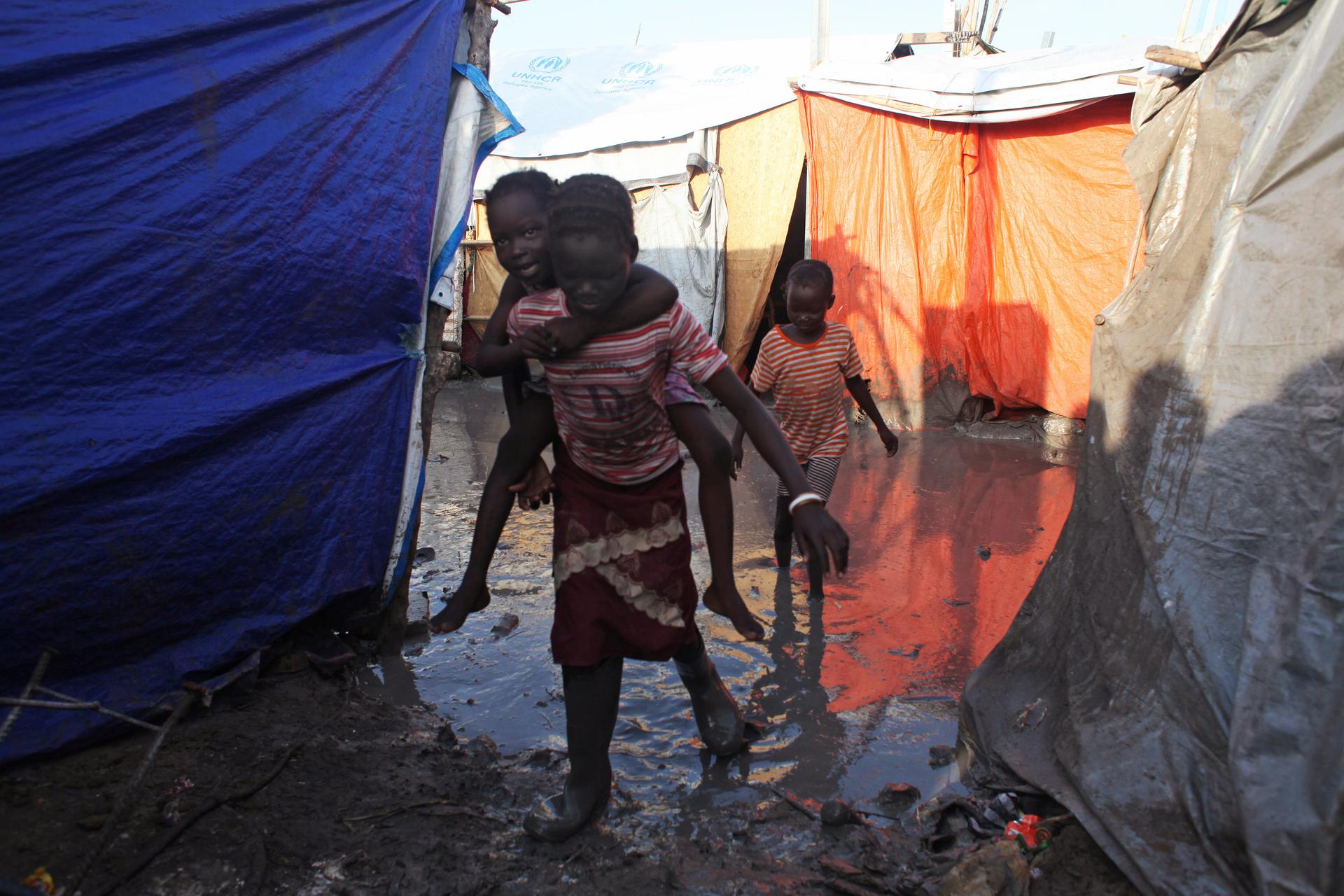 A South Sudanese girl displaced by the conflict carries a younger boy on her back as they walk through mud in a flooded camp for internally displaced people at the UNMISS base in Malakal, Upper Nile State May 30, 2014. There are about 18,000 people shelte