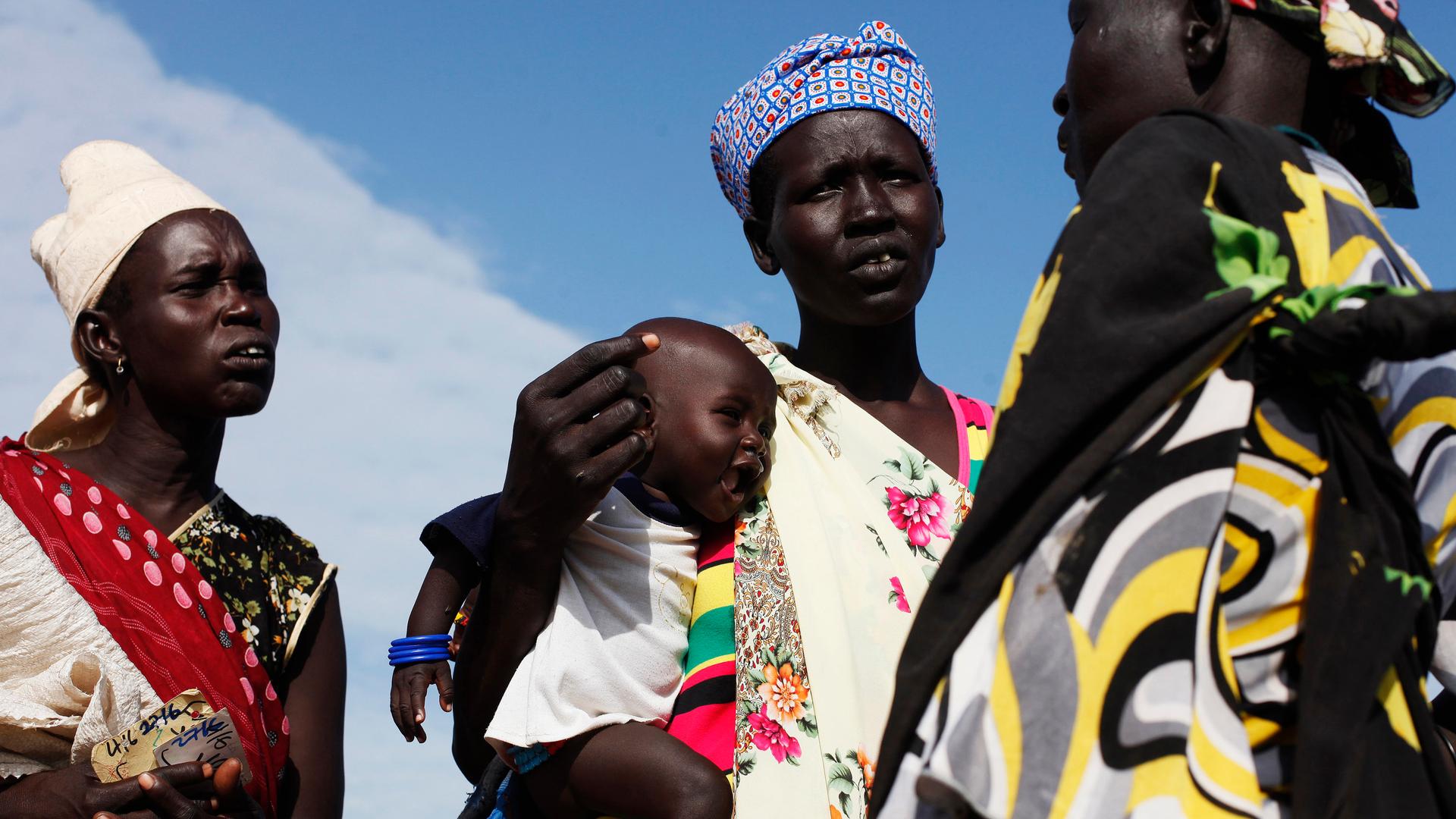 A woman carries a baby as she talks with other women at a food distribution in Minkaman, South Sudan. 
