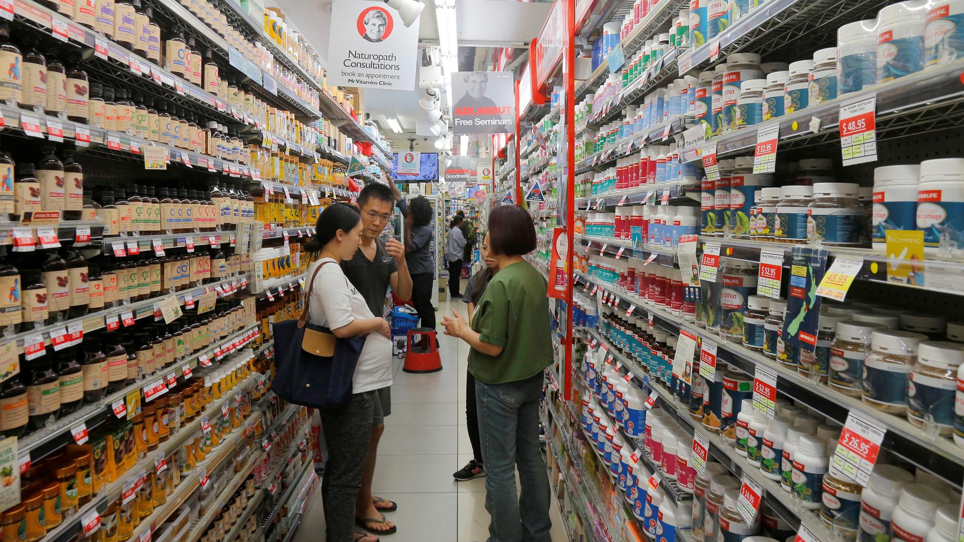 Shoppers are in an aisle of a health store looking at a wide variety of supplements.
