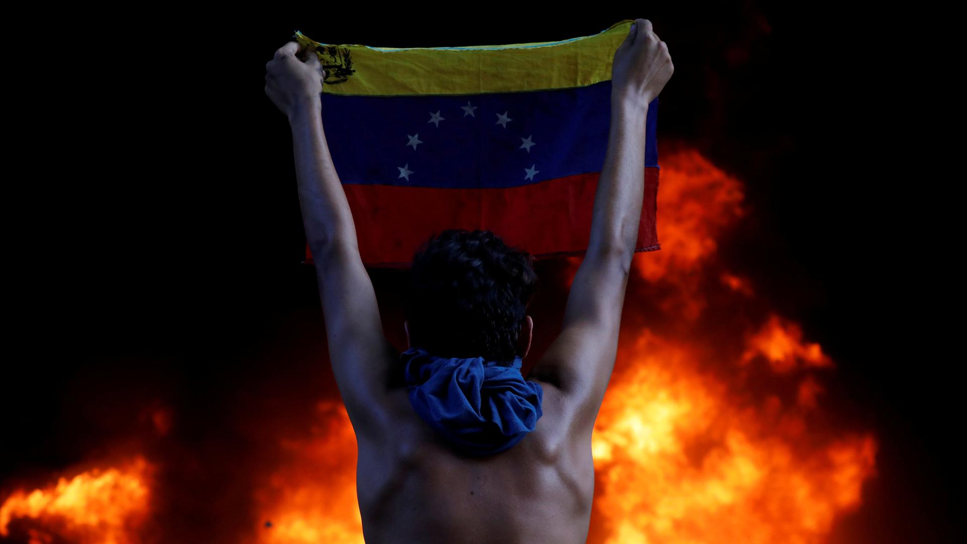 A protester holds a national flag while standing in front of a fire burning at the entrance of a building housing the magistracy of the Supreme Court of Justice, during a rally against Venezuela's President Nicolas Maduro, in Caracas, Venezuela, June 12, 