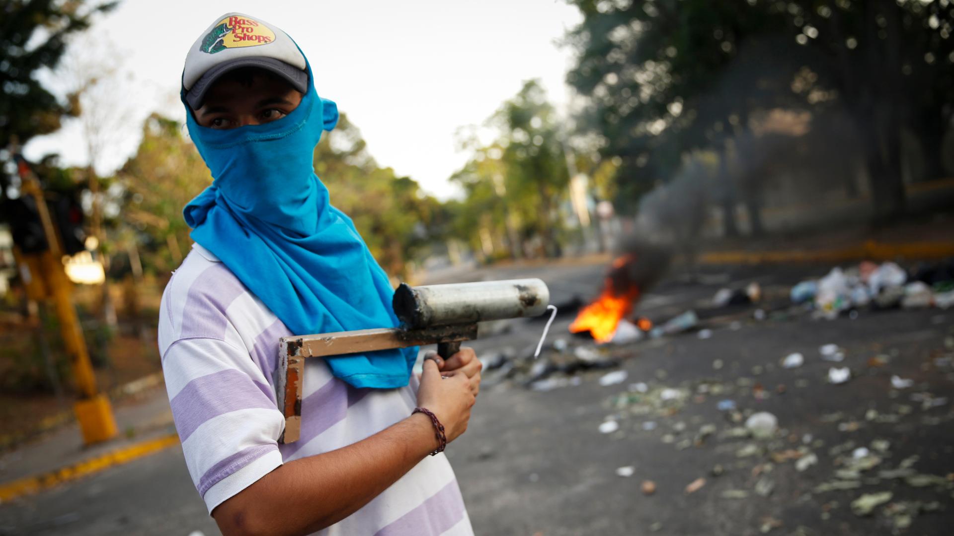 A demonstrator stands guard with a rudimentary mortar in front of a burning barricade during protests against Nicolás Maduro's government in San Cristóbal, Venezuela.