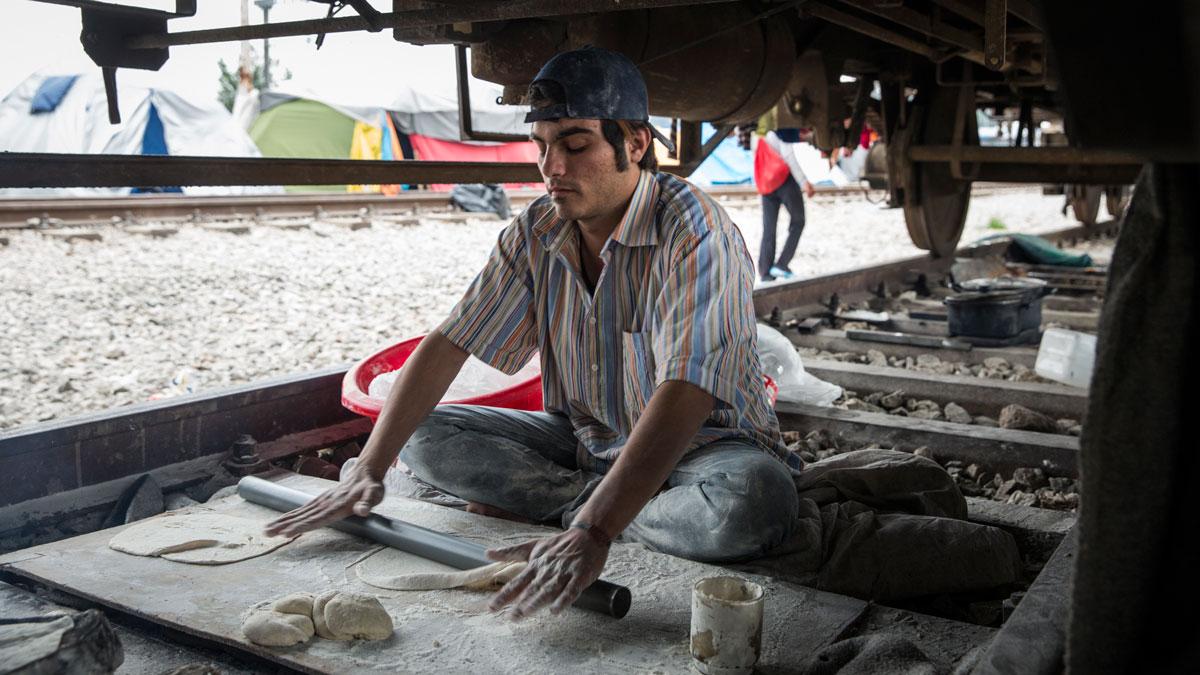Makmoud Nakarch rolls out dough in order to make Syrian flatbread in his bakery under a cargo train parked at Idomeni Camp.