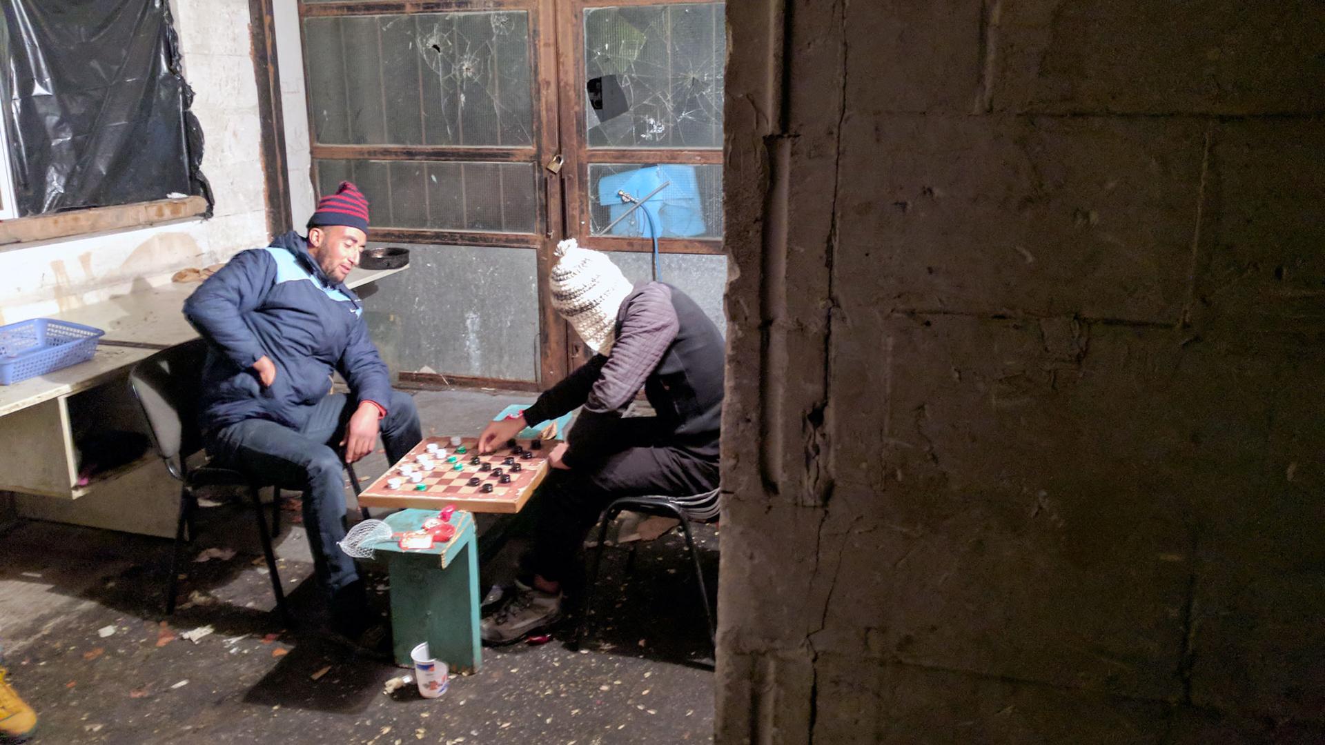 Two migrants play checkers with bottle caps in an abandoned warehouse where they live on the Greek island of Lesbos. 