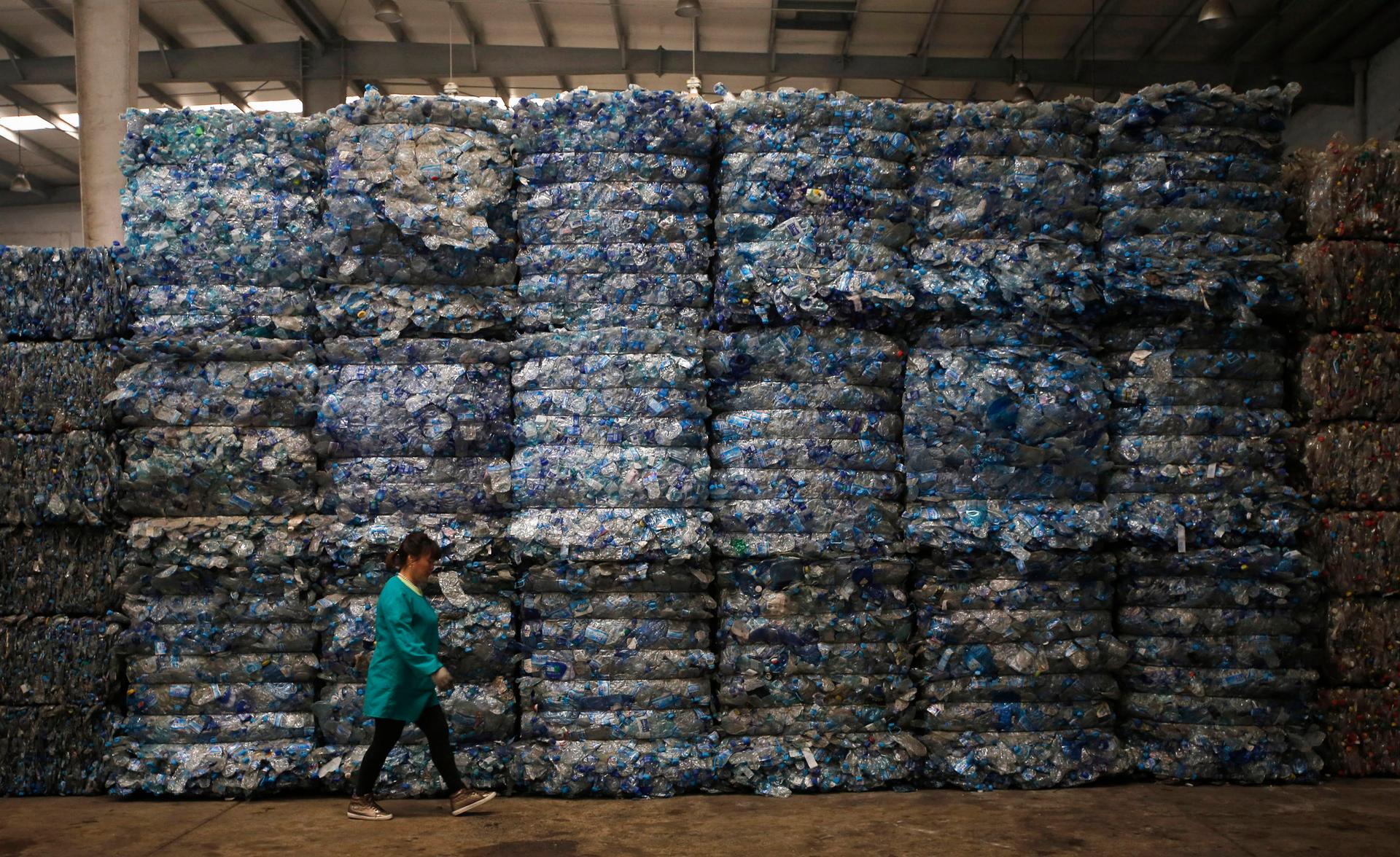 A worker walks past piles of plastic PET bottles at Asia's largest PET plastic recycling factory