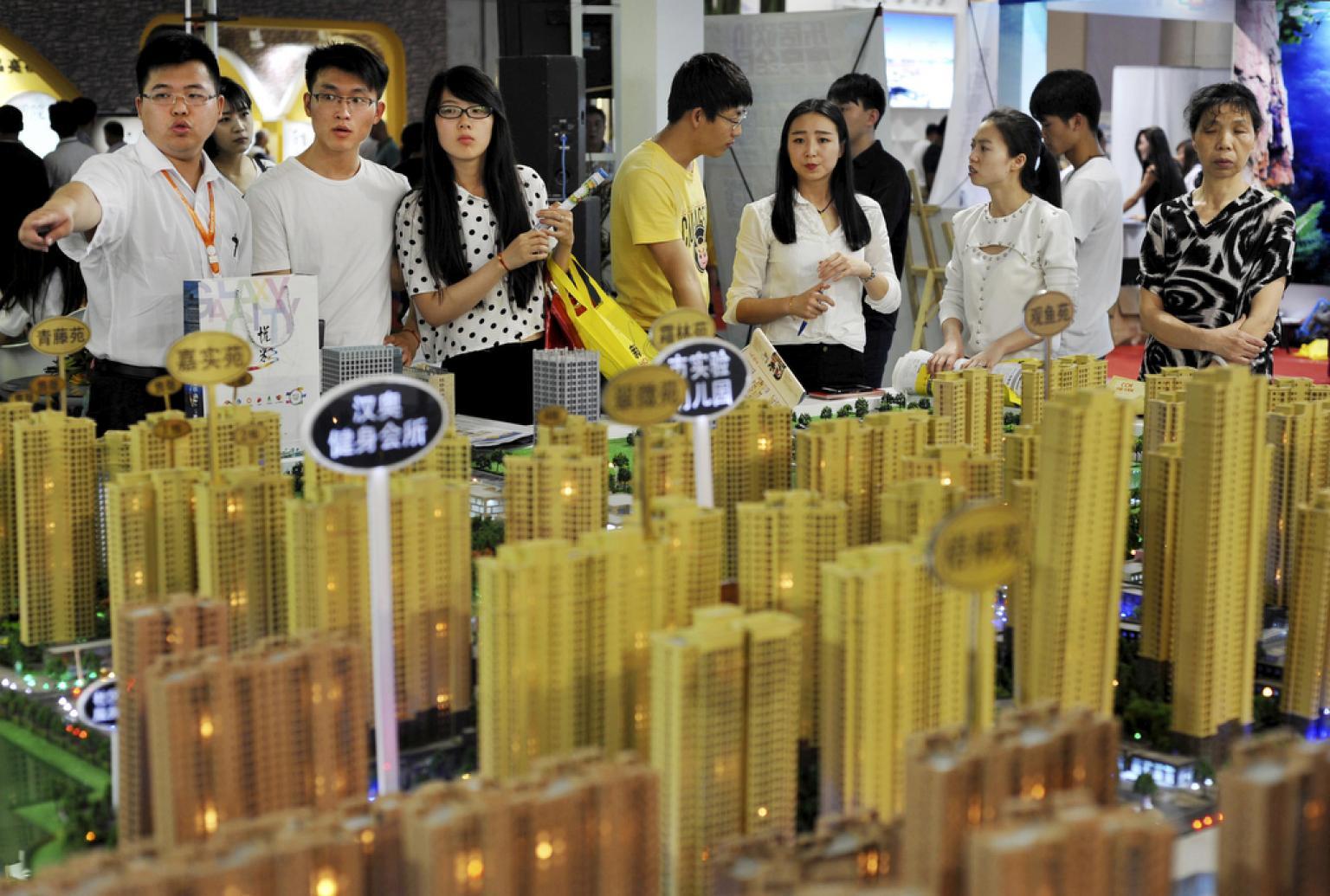 Sales representatives talk to potential buyers in front of a model of a residential complex at a real estate exhibition in Wuhan, Hubei province, China, on May 10, 2015. 