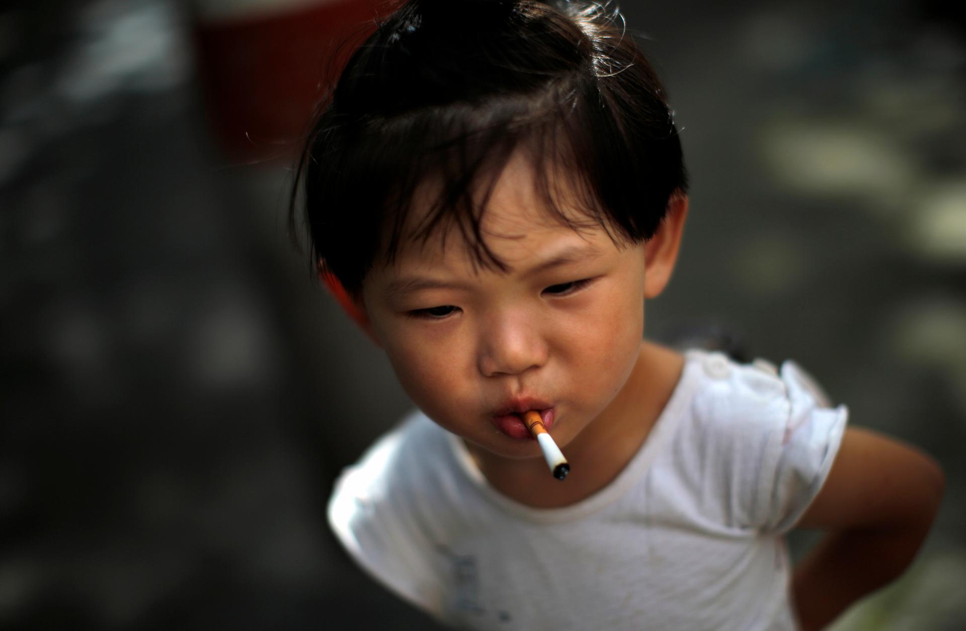 A small girl holds an unlit cigarette in her mouth