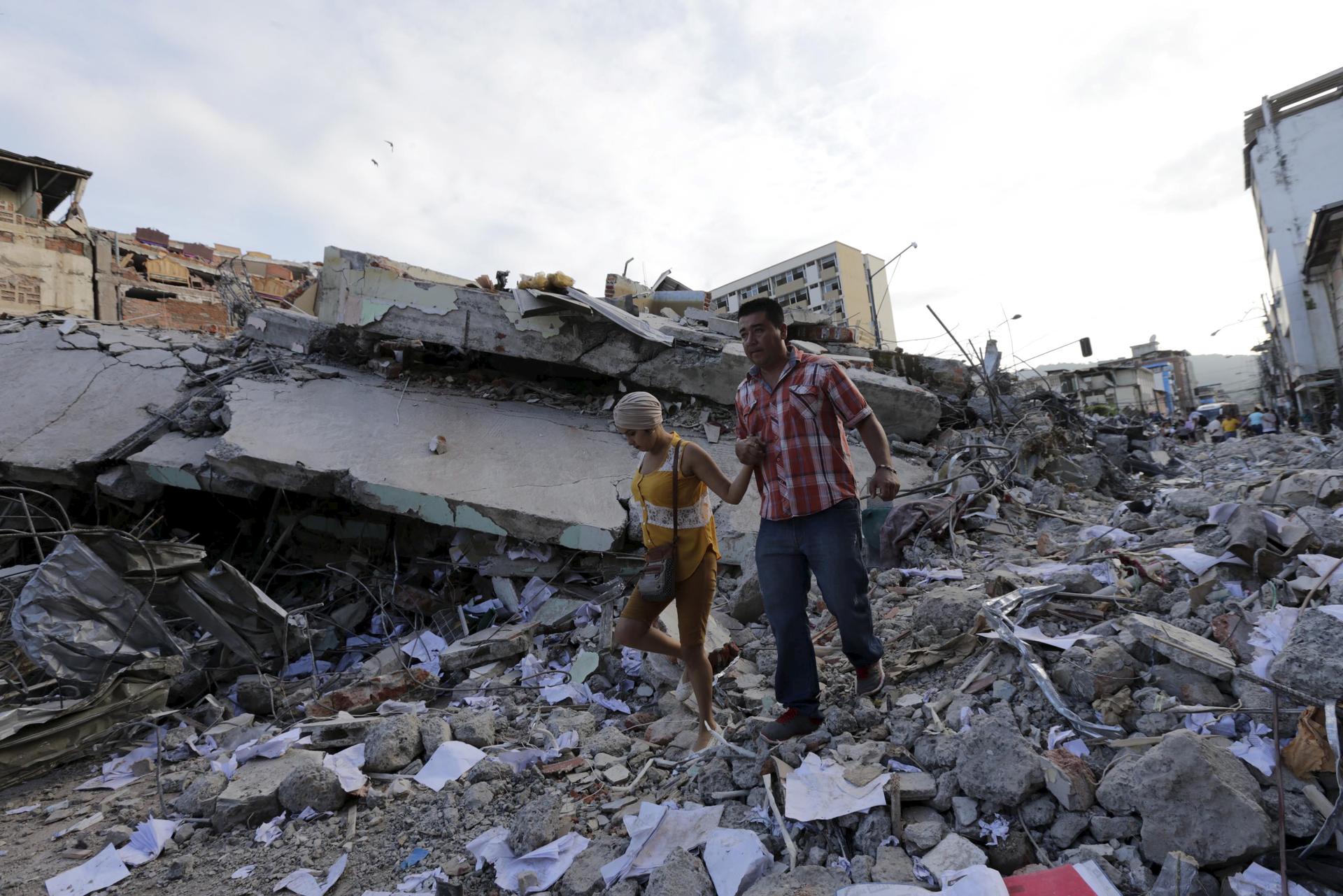 People walk past debris of a collapsed building