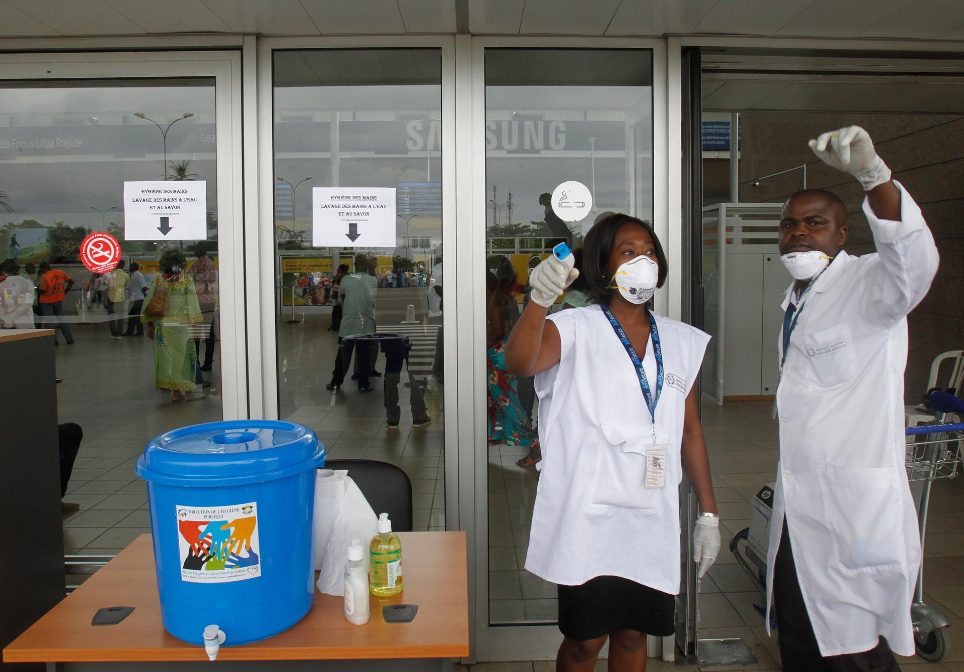 Health workers wearing protective masks and gloves gesture as they talk at the Felix Houphouet Boigny international airport in Abidjan August 12, 2014.