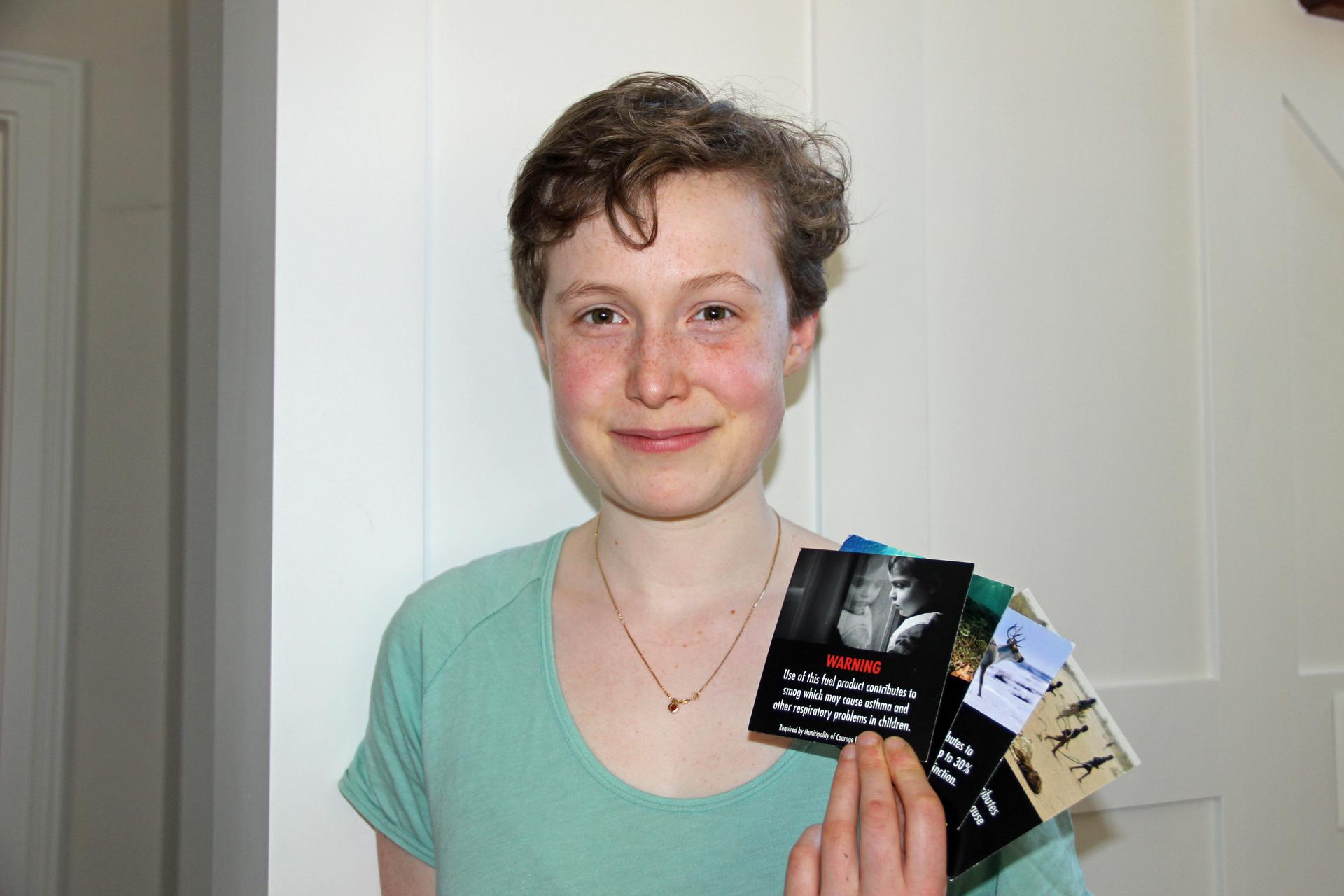 Environmentalist Emily Kelsall holds up samples of gas pump labels.