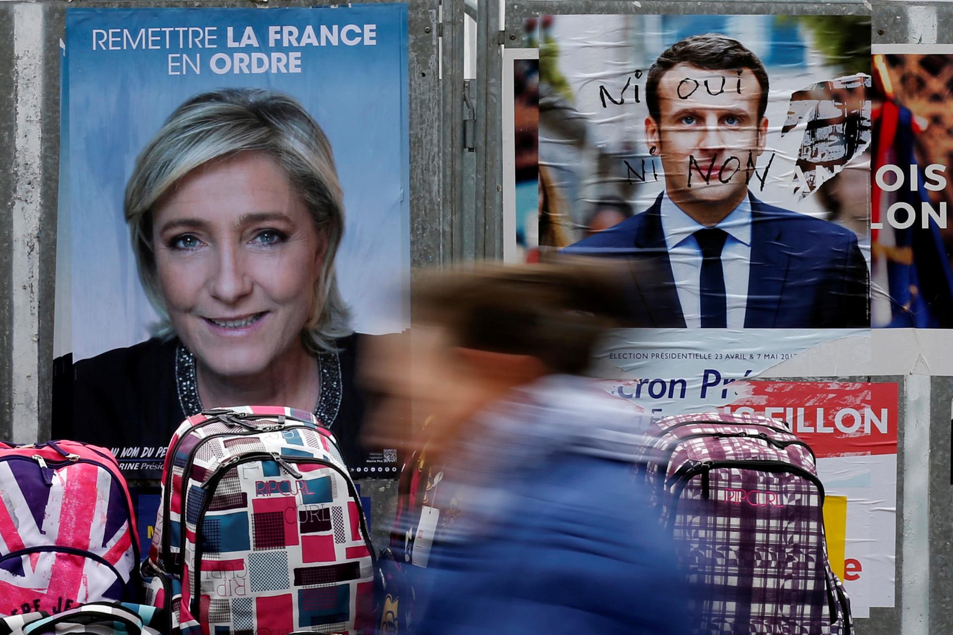 A woman walks past official posters of candidates for the 2017 French presidential election Marine Le Pen and Emmanuel Macron
