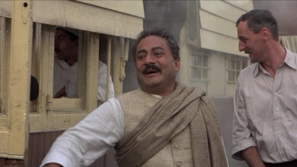A screen shot from Gandhi with extra Aseem Chhabra as a passenger in the background on the train. In the foreground is Saeed Jaffrey (left) as Sardar Patel and Gunter Maria Halmer playing Herman Kallenbach.