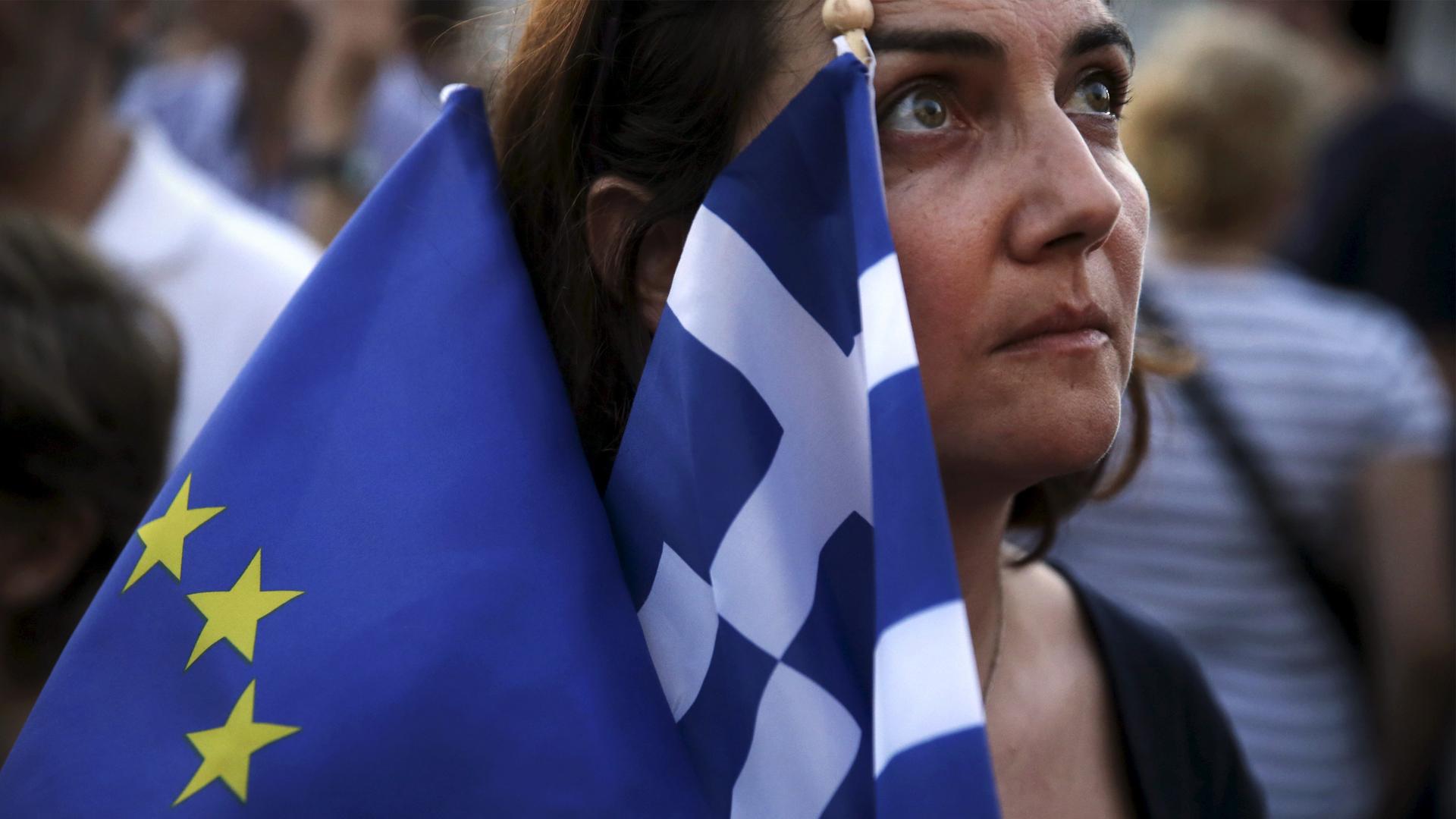 A pro-Euro protester holds a European Union and a Greek national flag during a rally in front of the parliament building in Athens, Greece, July 9, 2015.