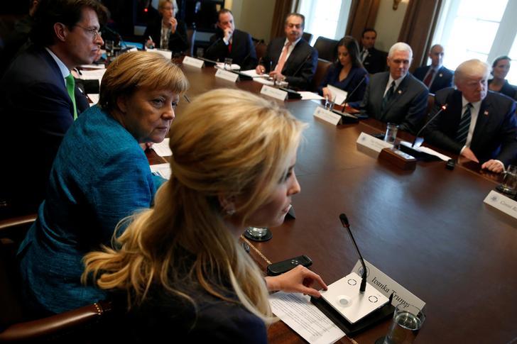 German Chancellor Angela Merkel sits to the left of Ivanka Trump, their backs facing the camera as they address President Donald Trump and a full table of German and American business leaders during a roundtable conversation at the White House on March 17