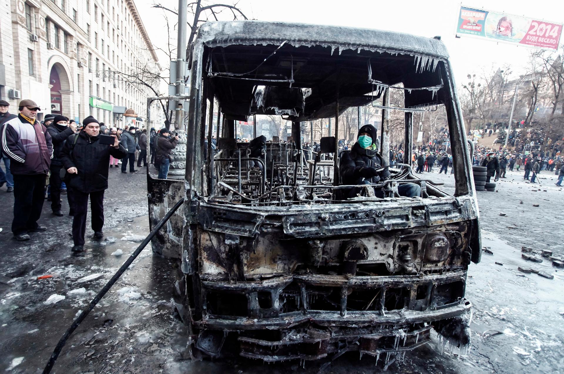 A pro-European integration protester sits in a burnt police bus after a rally near government administration buildings in Kiev January 20, 2014. With tension still high, about 1,000 protesters confronted police on Monday near Kiev's main government headqu