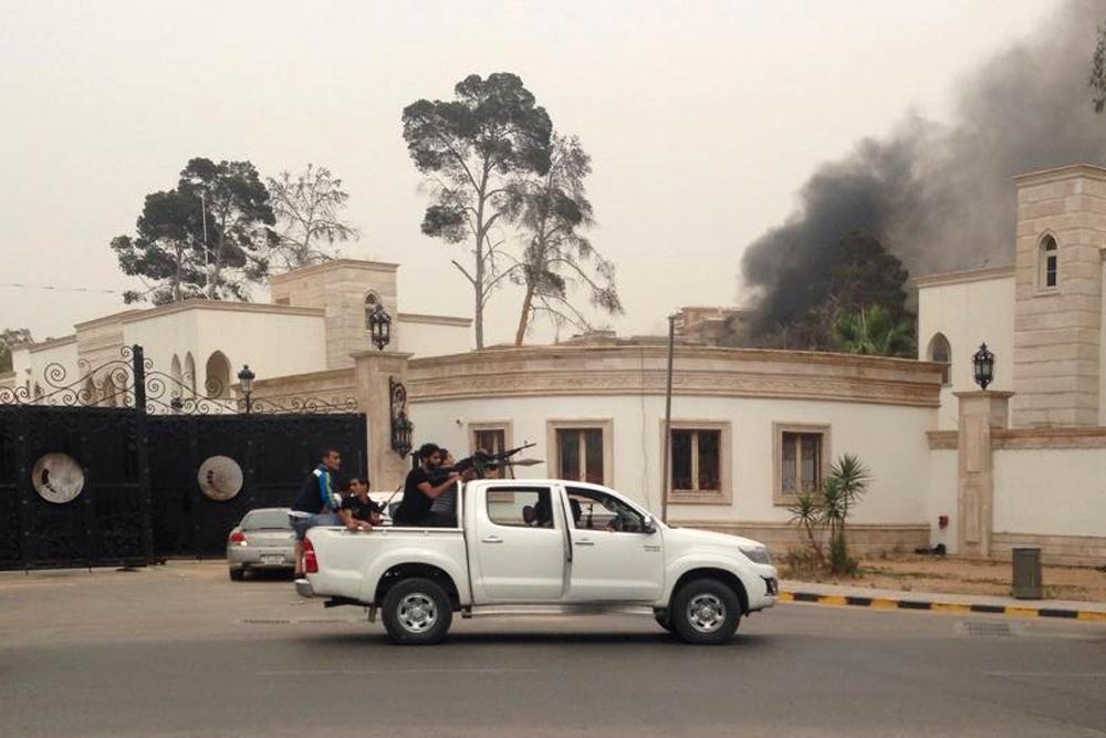 Armed men aim their weapons from a vehicle as smoke rises in the background near the General National Congress in Tripoli May 18, 2014. Heavily armed gunmen stormed into Libya's parliament on Sunday after attacking the building with anti-aircraft weapons