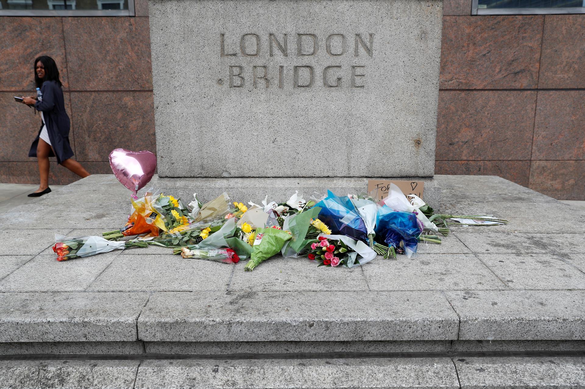 A woman passes flowers left on the south side of London Bridge