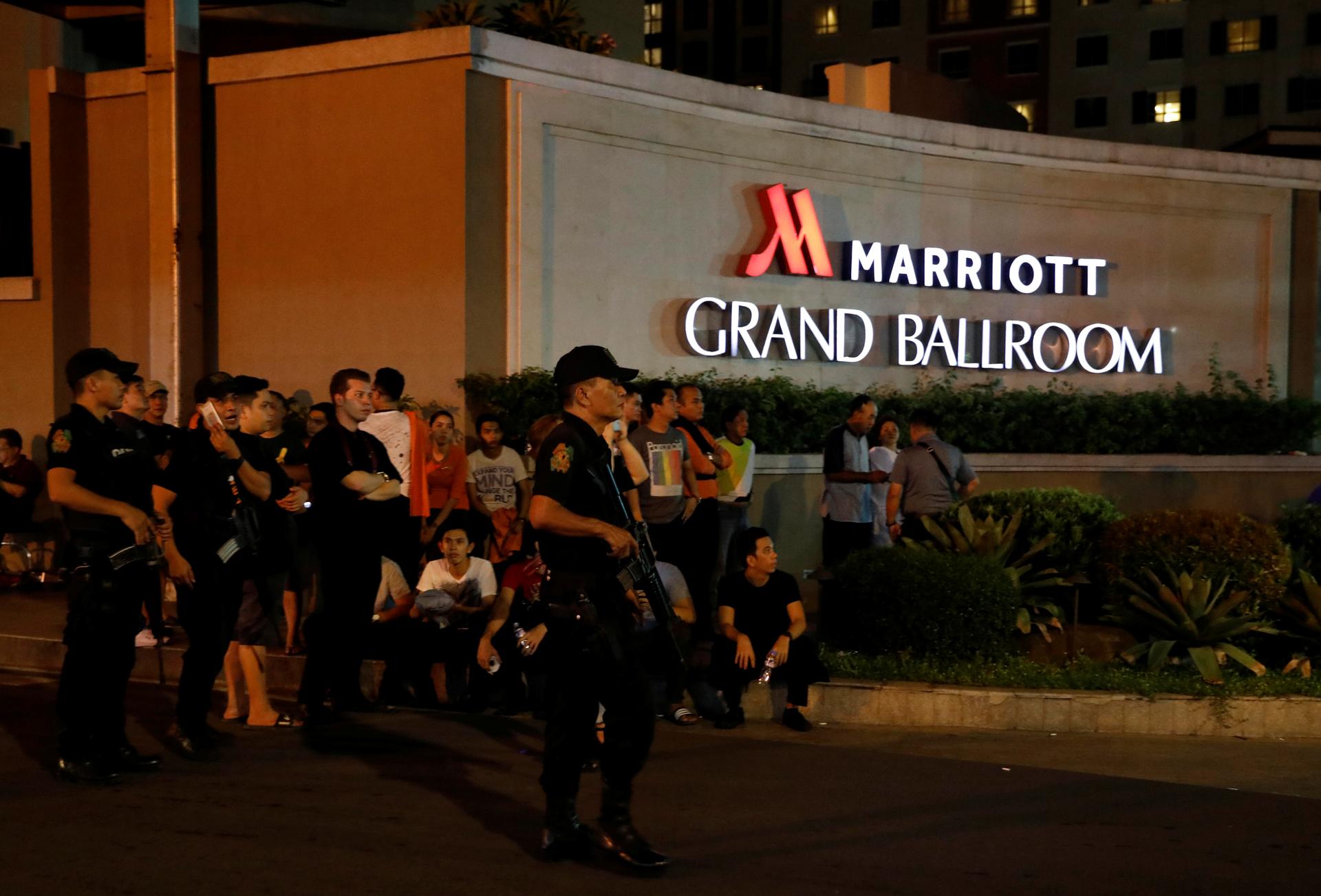 Policemen stand guard near evacuated employees of a hotel near a situation at a Resorts World building, in Pasay City, Metro Manila, Philippines.