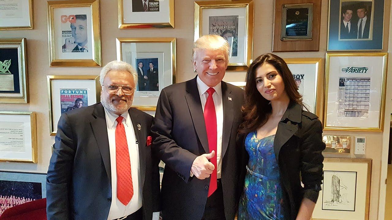 A man and a woman pose with Donald Trump in an office
