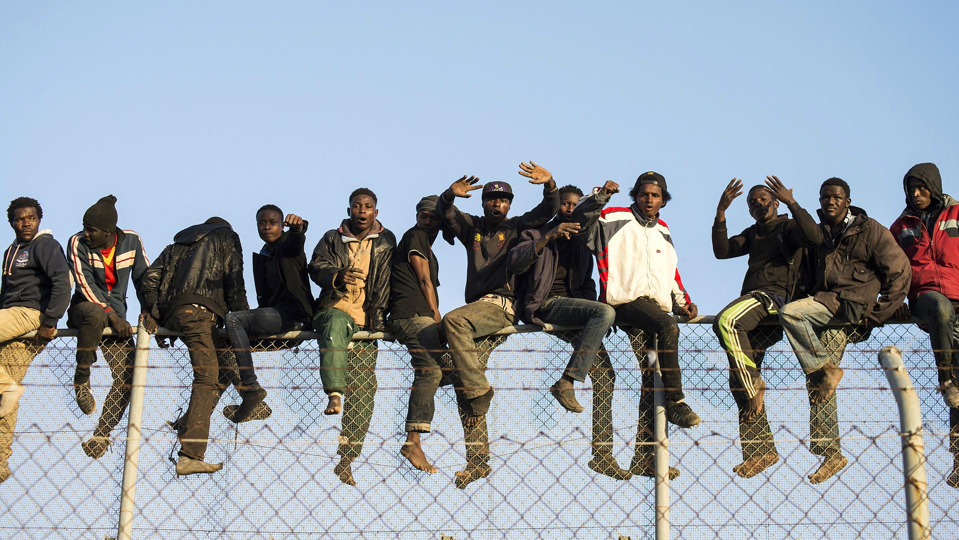 African migrants sit atop a border fence during an attempt to cross into Spanish territories, between Morocco and Spain's north African enclave of Melilla, Oct. 22, 2014.