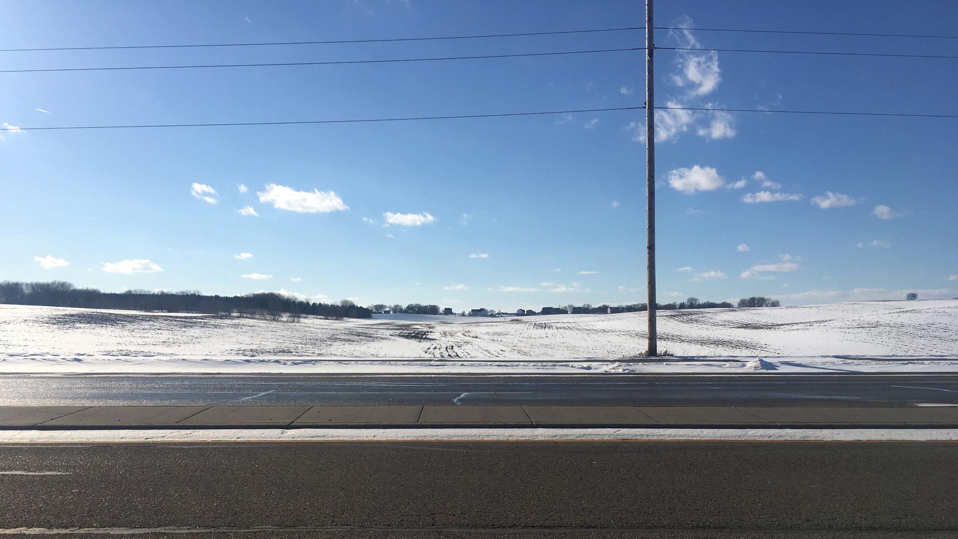 Sunshine on an empty road with snow-covered farmland in the background
