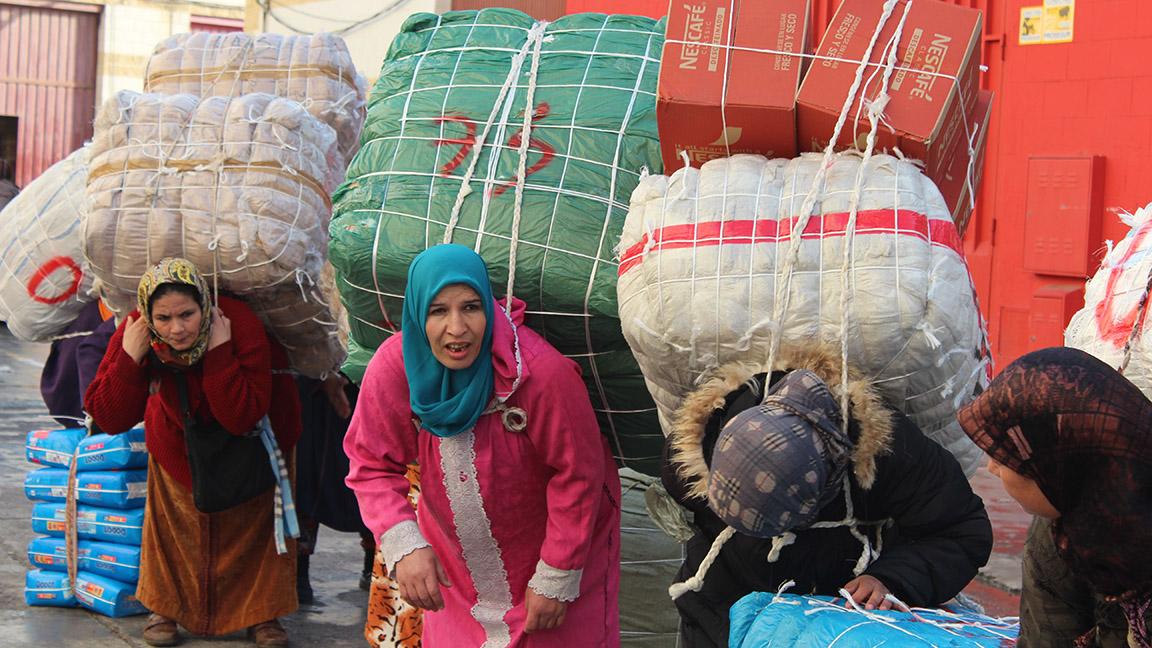 Moroccan women wait at a border crossing with loads of 100-200 pounds of commercial goods on their backs.