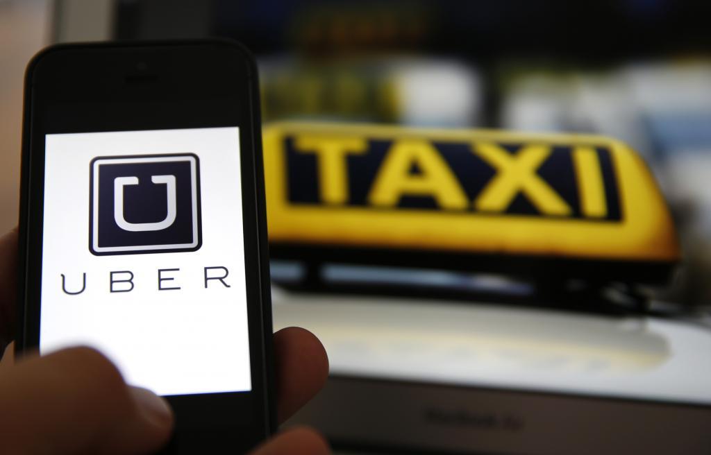 An illustration picture shows the logo of car-sharing service app Uber on a smartphone next to the picture of an official German taxi sign in Frankfurt, September 15, 2014. 