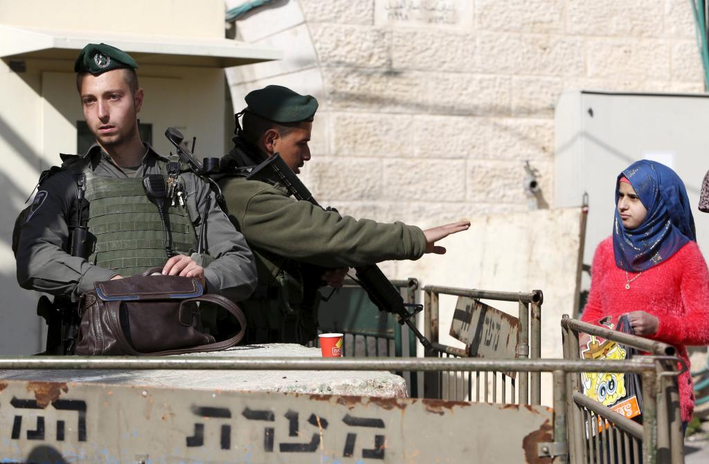 An Israeli border policeman gestures to Palestinians as another searches a bag in the West Bank city of Hebron