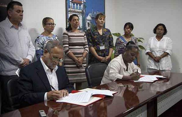 Scott Gilbert (L) signs a business deal with Cuba representatives to buy 80 tons of artisanal marabu charcoal.