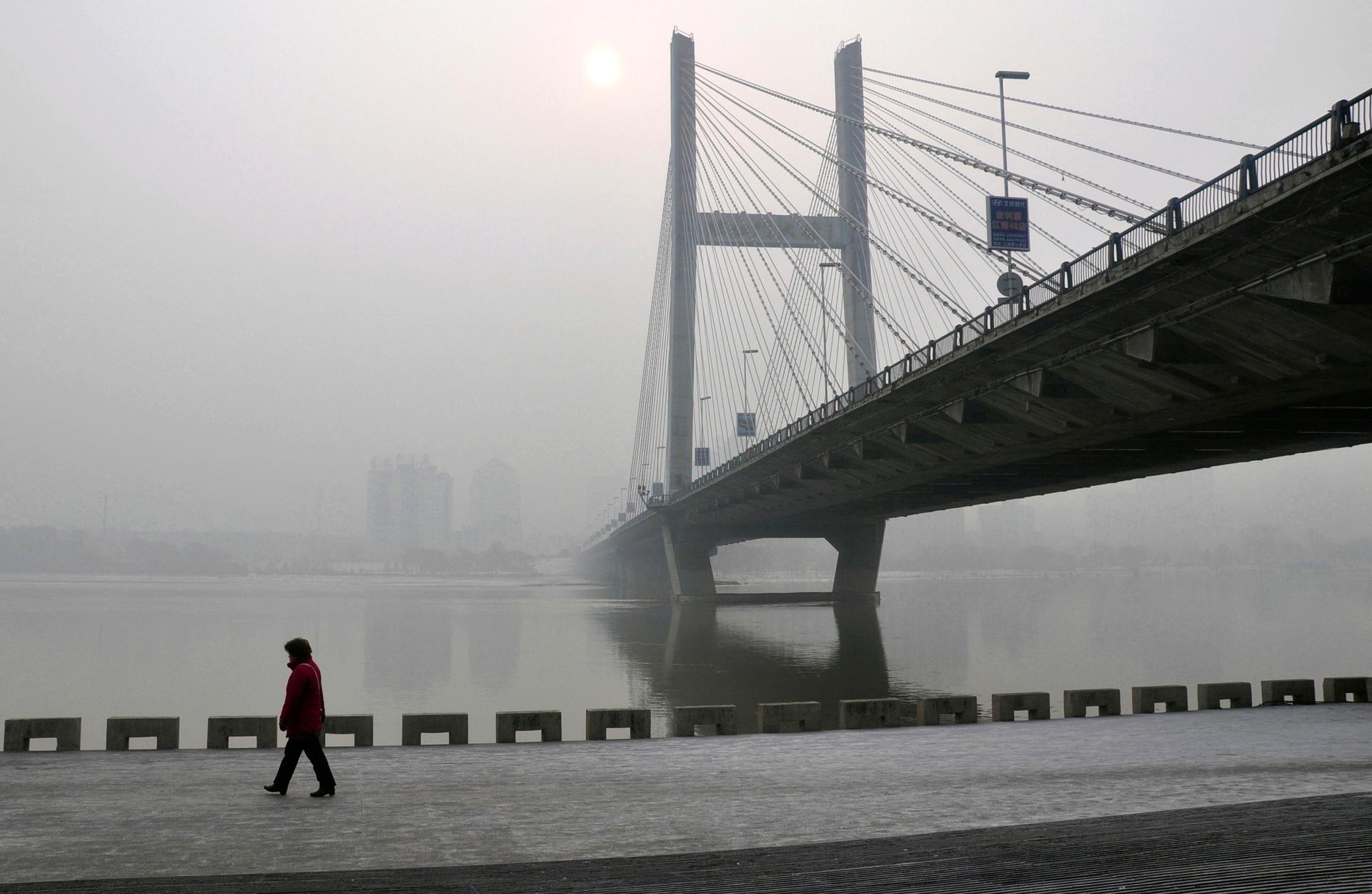 A resident walks along a street on the banks of the Songhua River near a highway bridge on a hazy day in Jilin, Jilin province, on February 25, 2014
