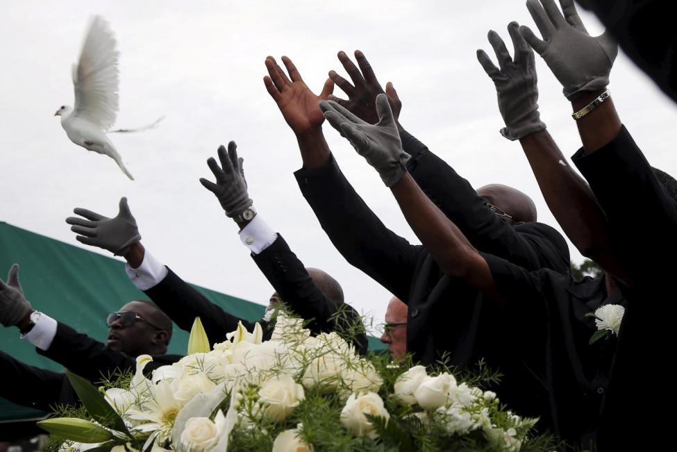 Pall bearers release white doves over the casket of a mass shooting victim