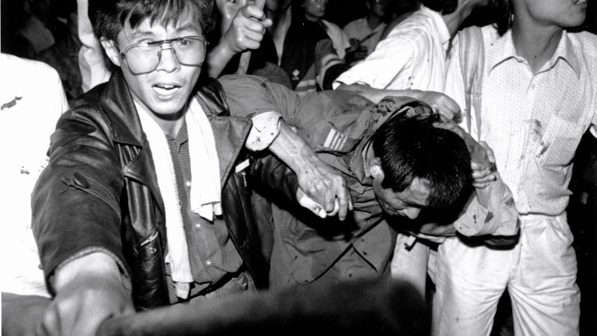 A captured tank driver is helped to safety by students as the crowd beats him on June 4, 1989. 