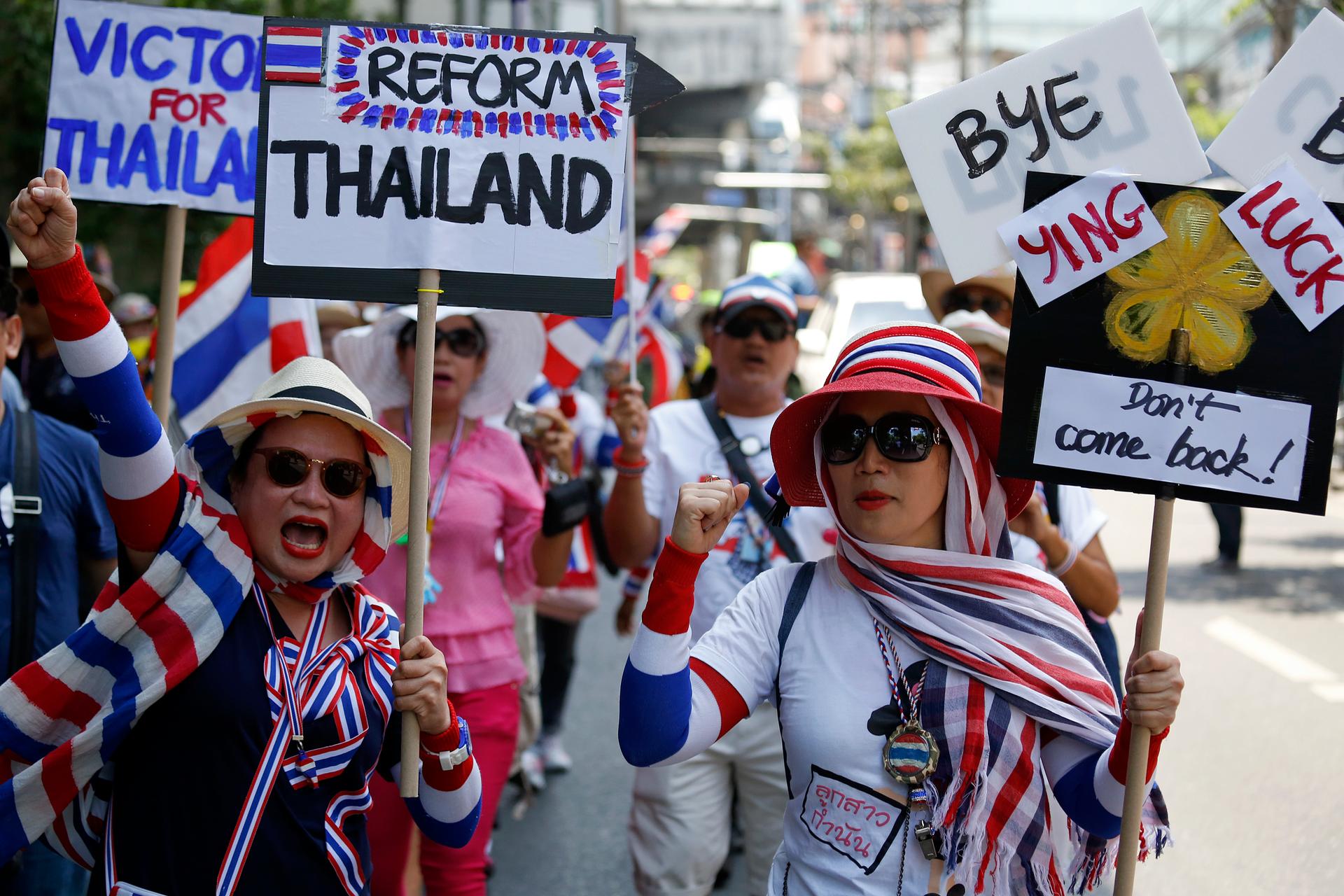 Anti-government protesters carry signs against ousted Prime Minister Yingluck Shinawatra as they march in central Bangkok May 8, 2014. Thailand's anti-corruption agency may decide on Thursday whether to pursue charges against Yingluck that could see her b