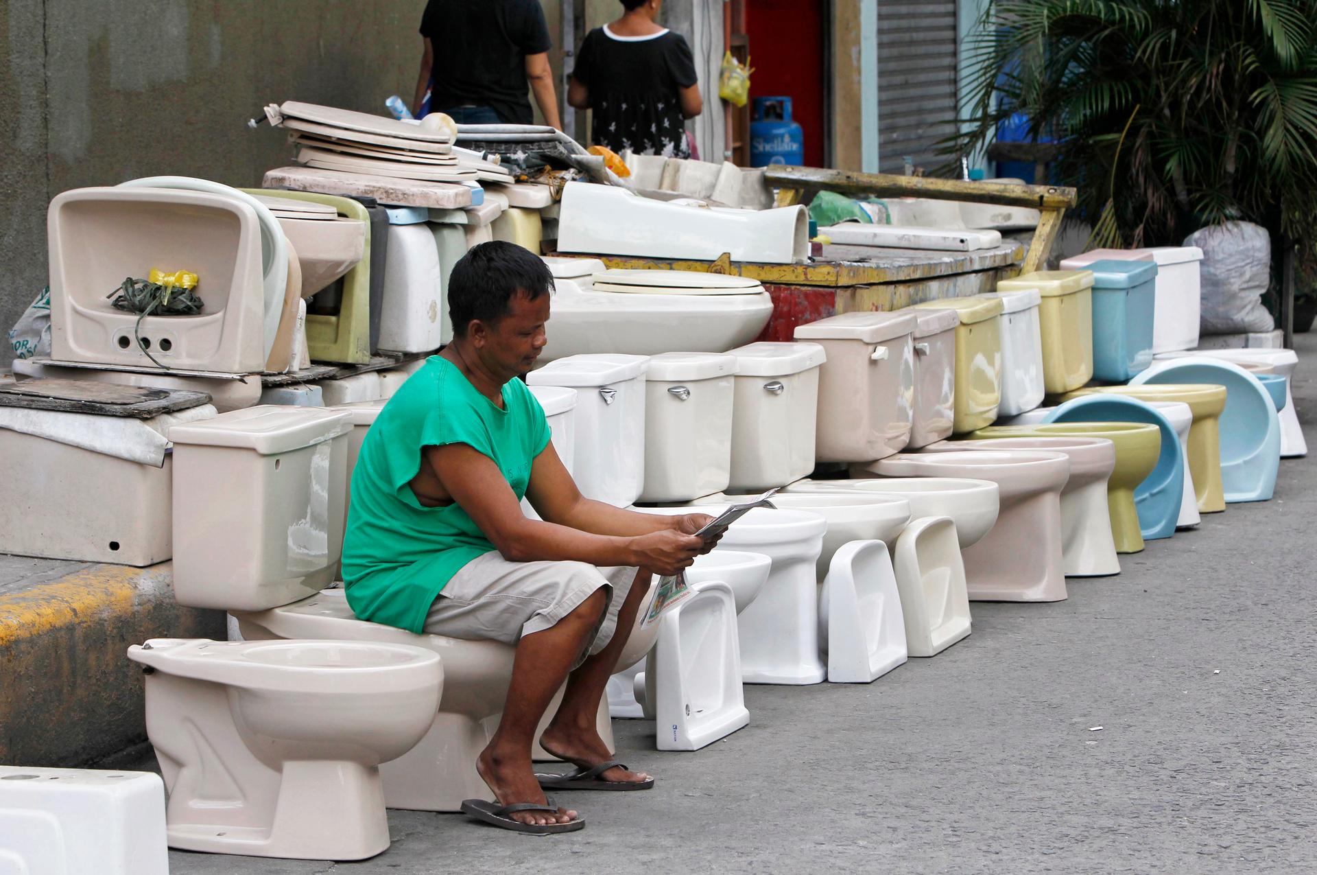 A man reads a newspaper while sitting on a second-hand toilet bowl he's selling in Manila, Philippines, on November 19, 2012.