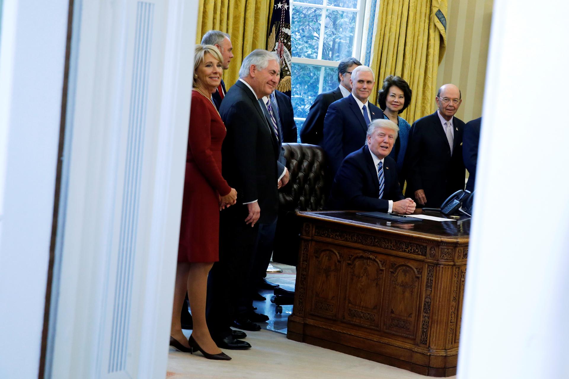 donald trump as seen through the double doors of the oval office surrounded by his advisers