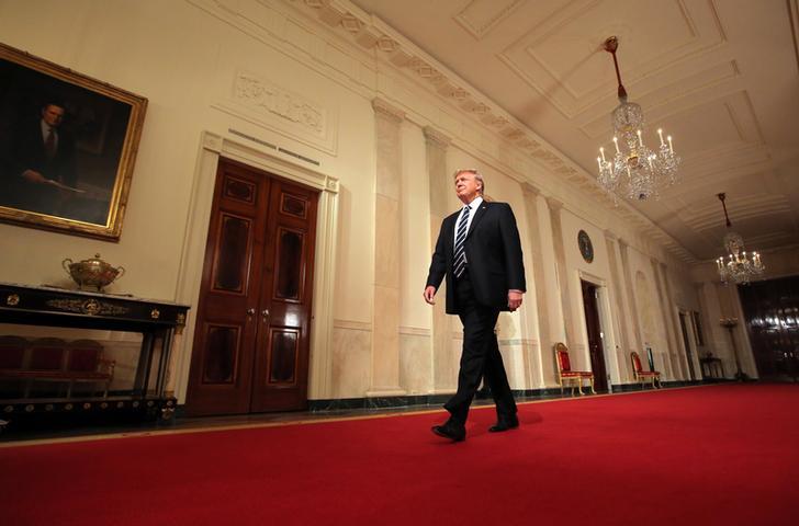 US President Donald Trump, with a grin on his face, walks down a bright red carpet in the White House.