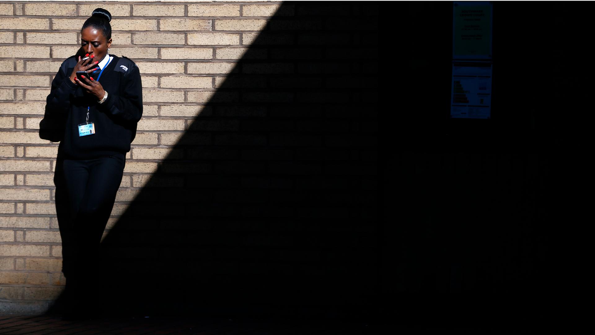 A security guard stands in the sunshine as she smokes outside Southwark Crown Court in central London, March 5, 2014.