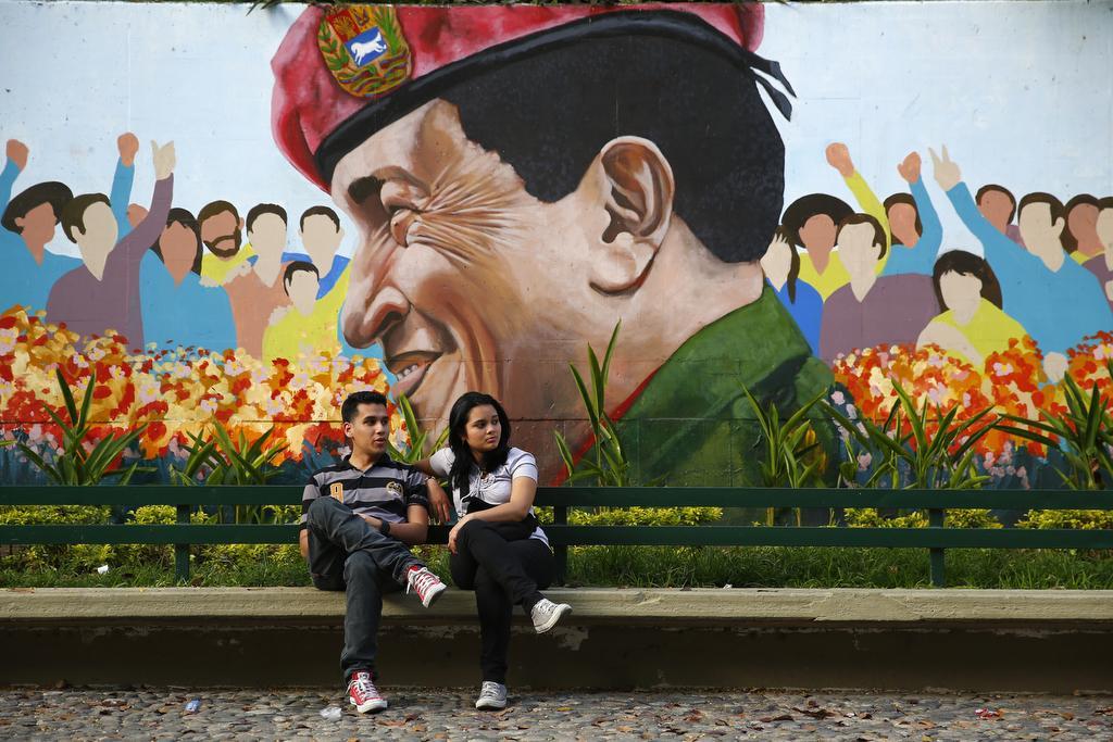 A couple sits in a park next to a mural of Venezuela's late President Hugo Chavez in Caracas on March 9, 2014.