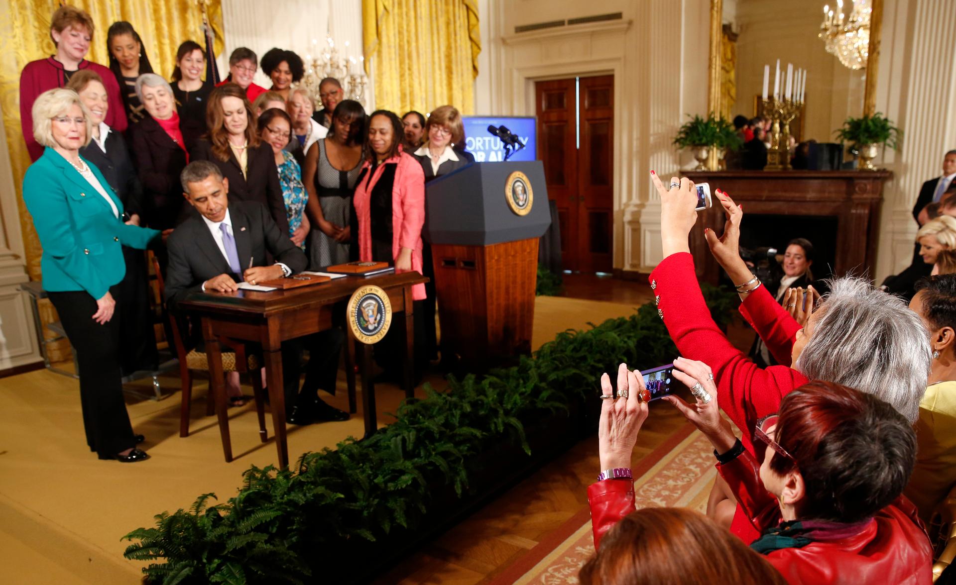 Women legislators take photos as US President Barack Obama signs two new executive actions