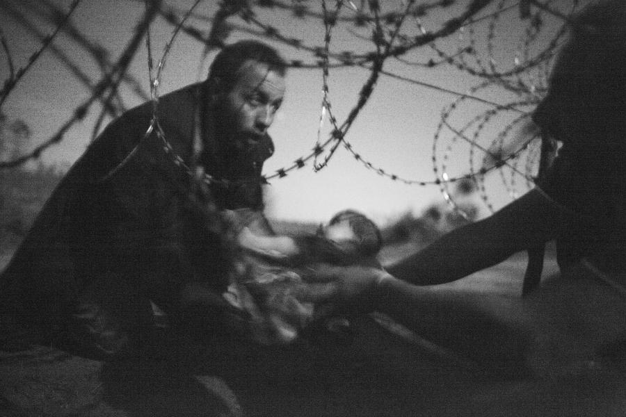 A man passes a baby through the fence at the Serbia/Hungary border in Röszke, Hungary, 28 August 2015.