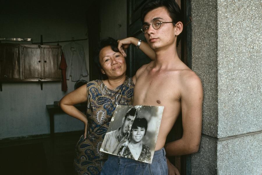 A mixed-race young man with a faded black and white photo of his parents: a handsome American GI and his Vietnamese bride.