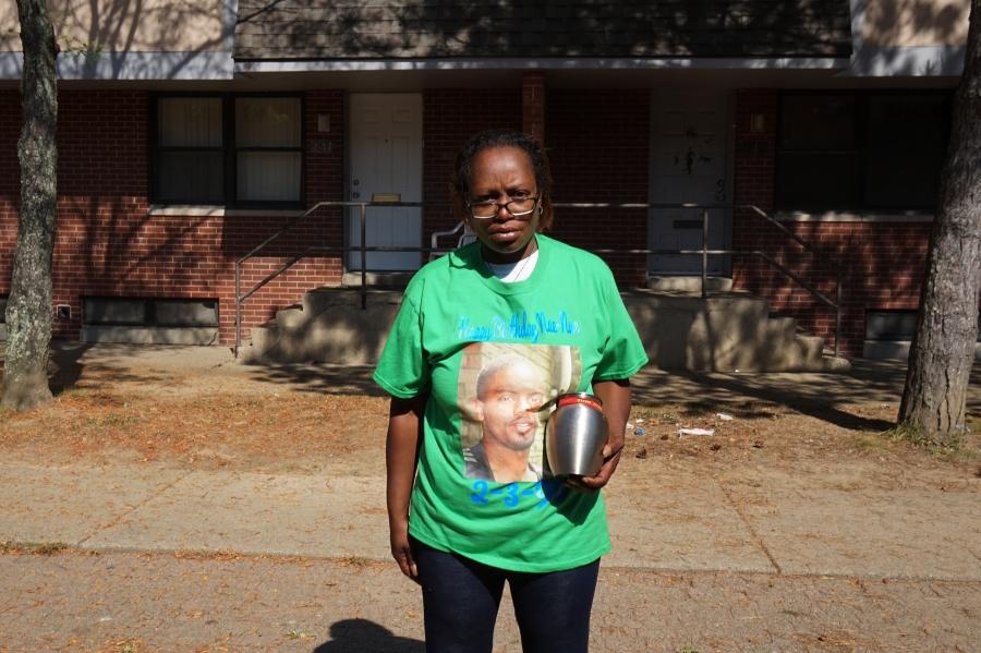 Woman in green T-shirt with man's face, holding urn